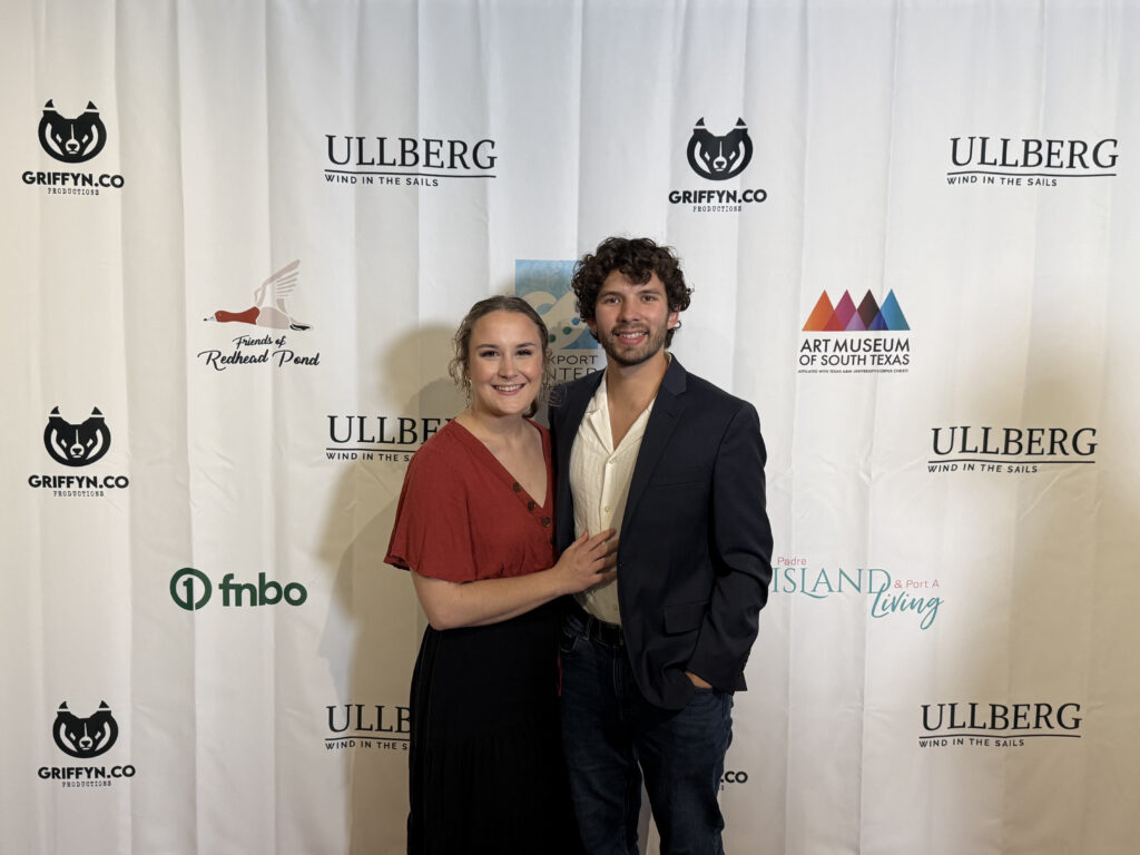 Couple posing on event red carpet with logos.