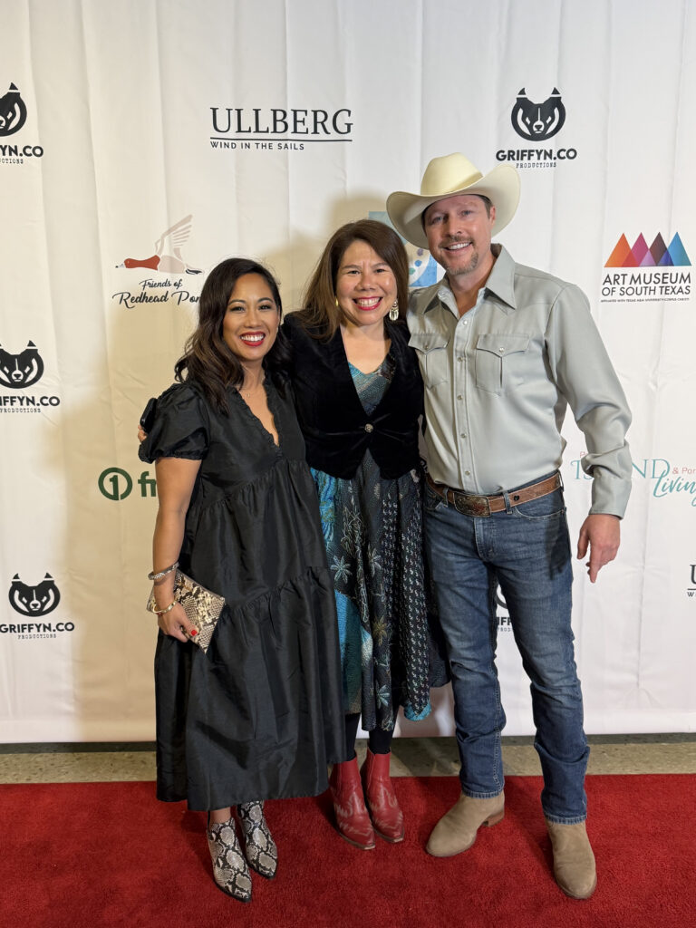 Three people smiling on red carpet event.