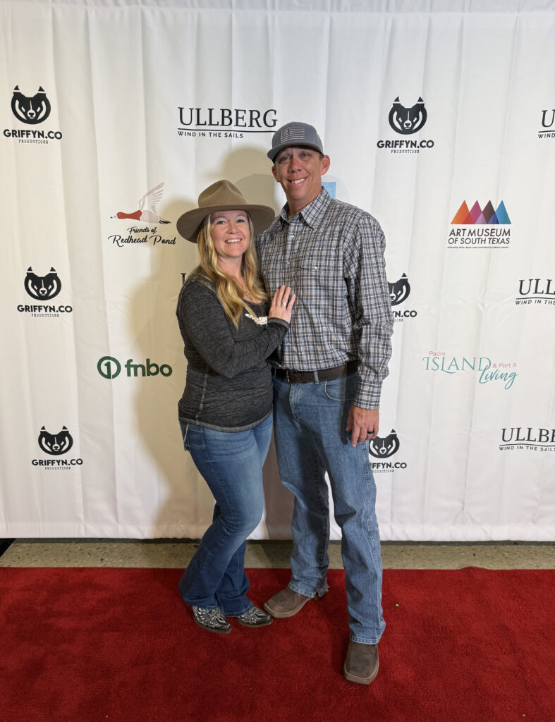 Couple smiling on red carpet at event backdrop.