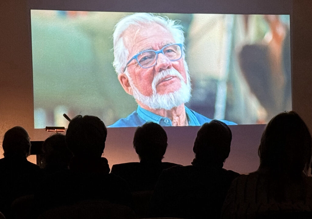 Audience watching movie of elderly man on screen