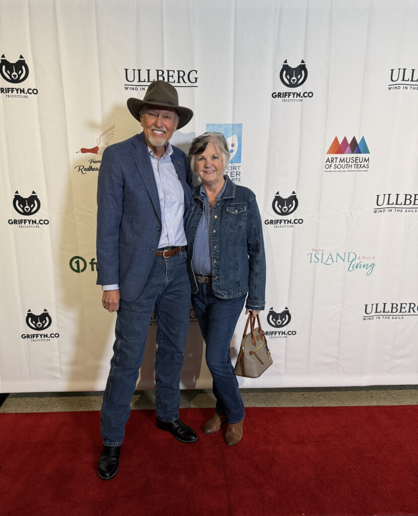 Couple posing on red carpet event backdrop.