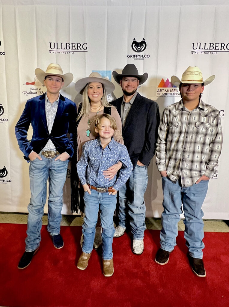 Family posing on red carpet in cowboy hats.