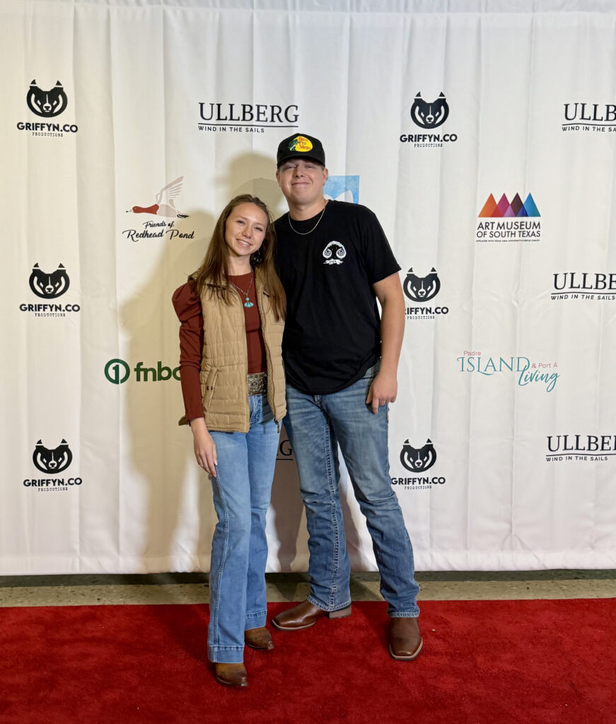 Two people posing on red carpet event backdrop.